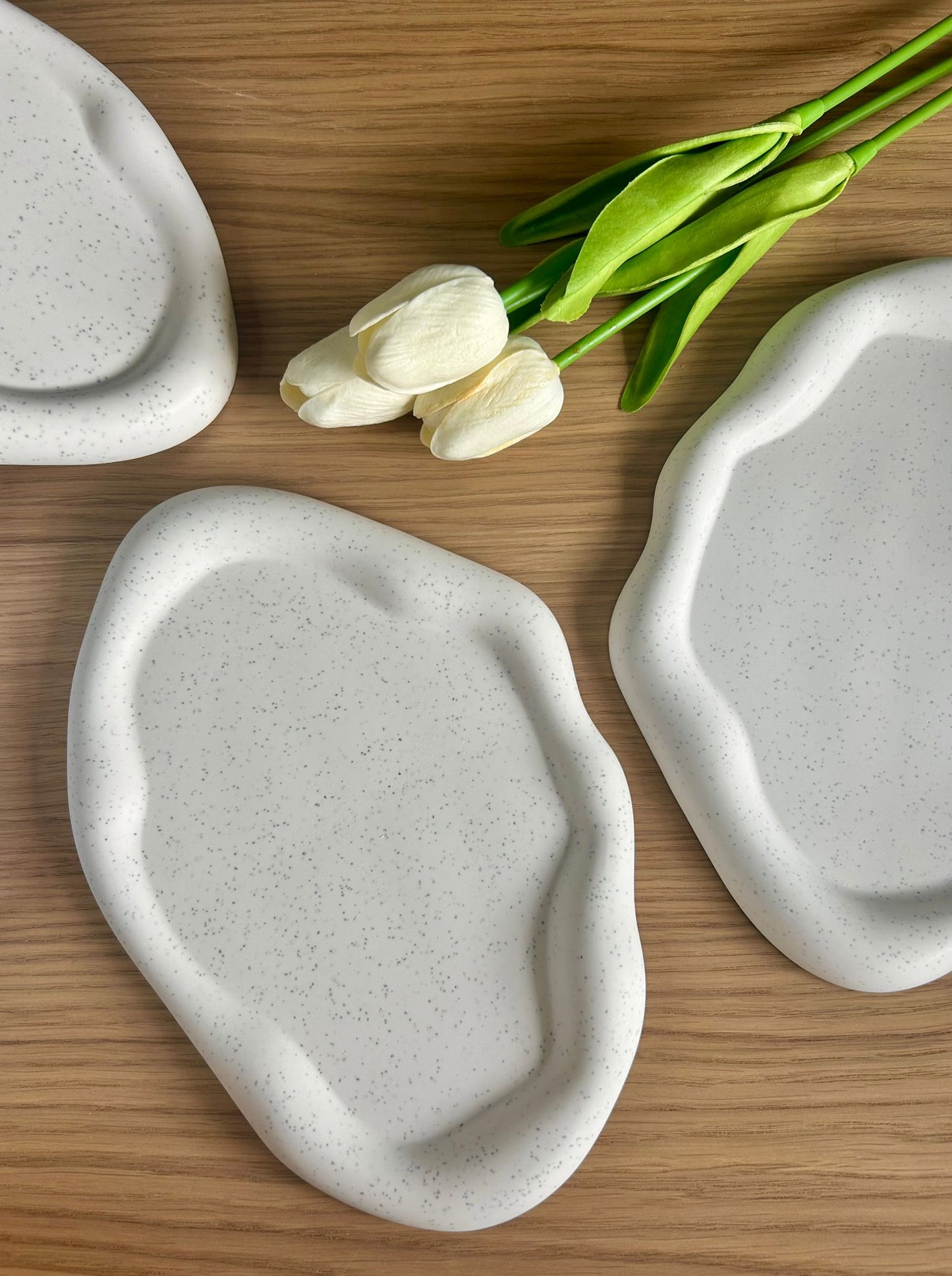 Flat lay of three speckled handmade Jesmonite trays on a wooden surface, part of the eco-conscious Calluna Collection of sustainable home accessories