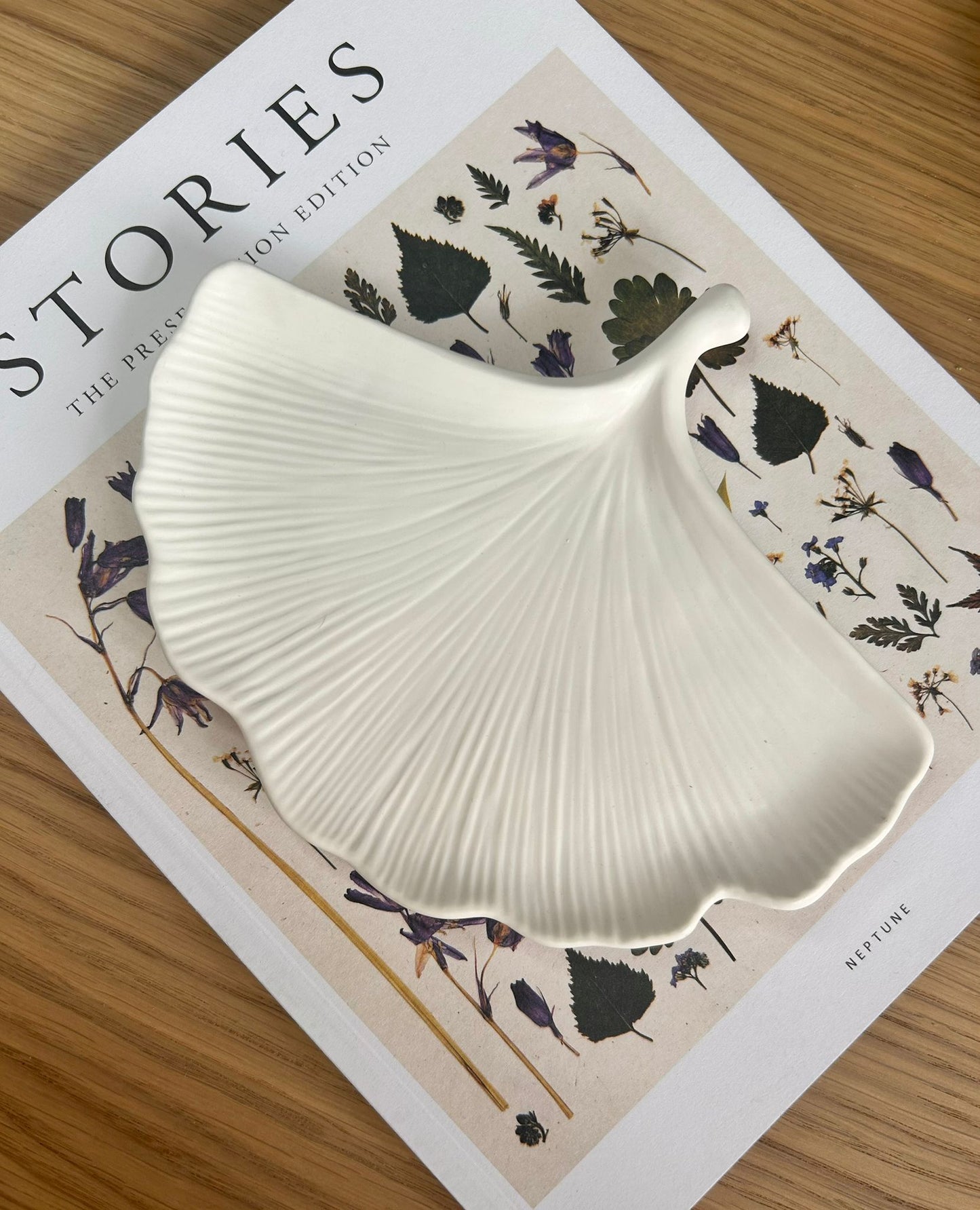 Handcrafted jesmonite tray shaped like a ginkgo leaf, styled on a floral-themed book. A sustainable, nature-inspired home accessory for conscious interiors.