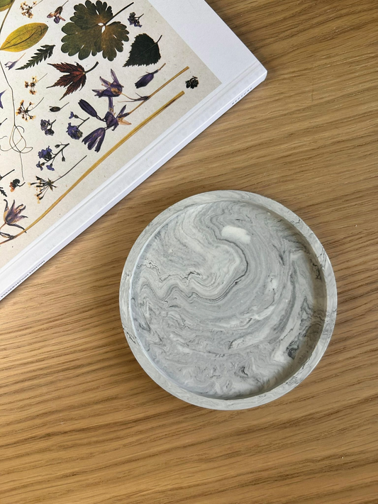 Round grey marbled coaster made from Jesmonite, styled on a wooden surface with a botanical book – minimalist handmade home accessory.