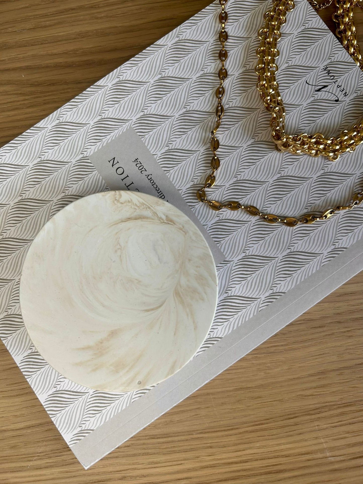 Creamy marbled coaster with soft neutral tones styled beside gold chain jewellery – minimal handcrafted home accessory.