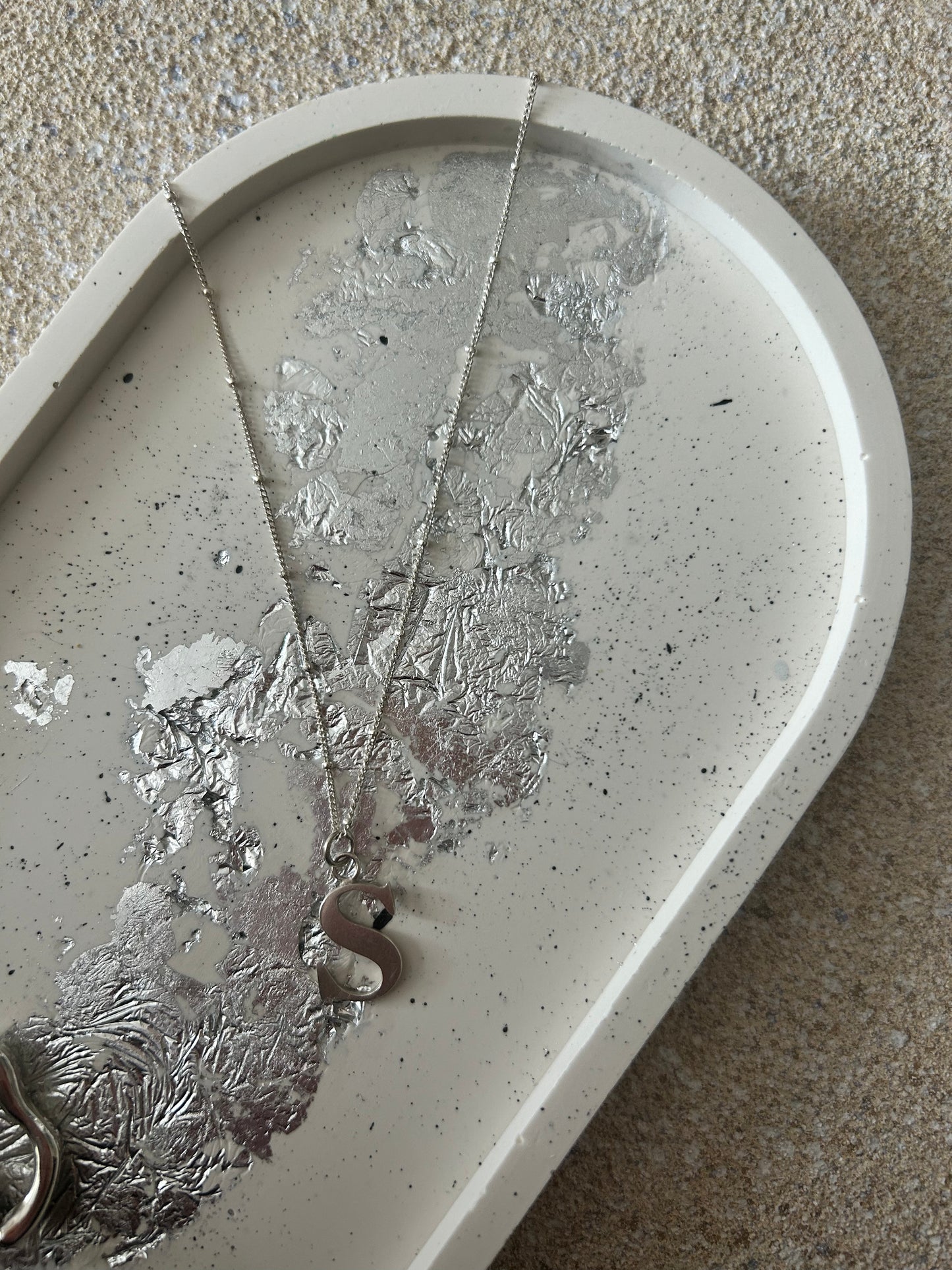 Handmade Home Accessories - Close of a Large oval cream trinket tray with black splatters and silver leaf detail. A silver necklace with a S charm is laid across it.