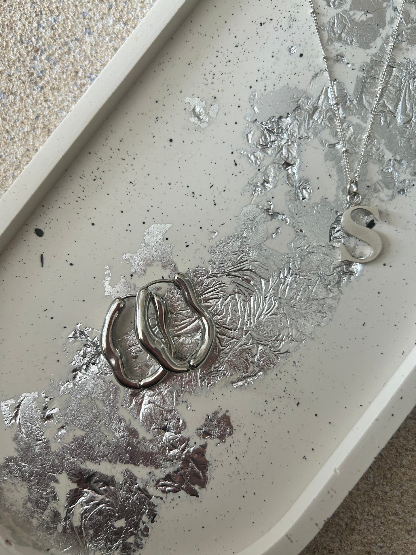 Handmade Home Accessories - A close up shot of a Large oval cream trinket tray with black splatters and silver leaf detail. Earrings and a silver necklace as on the tray for decorative purposes.