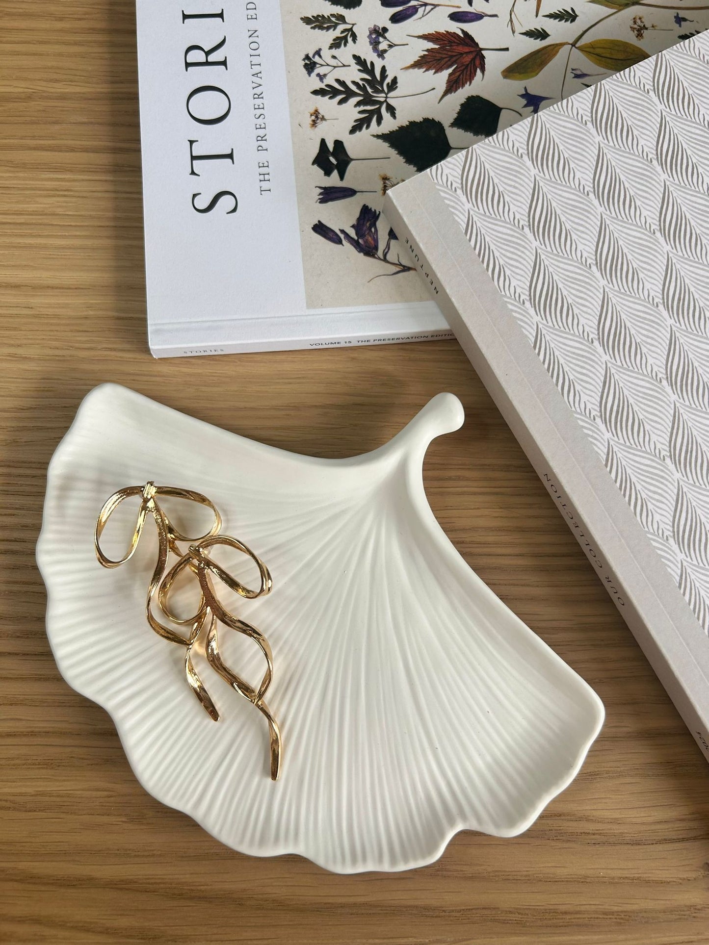 Leaf-inspired handmade home accessory in matte white ceramic, displayed with sculptural gold earrings – a minimalist tray for jewellery or decorative use.