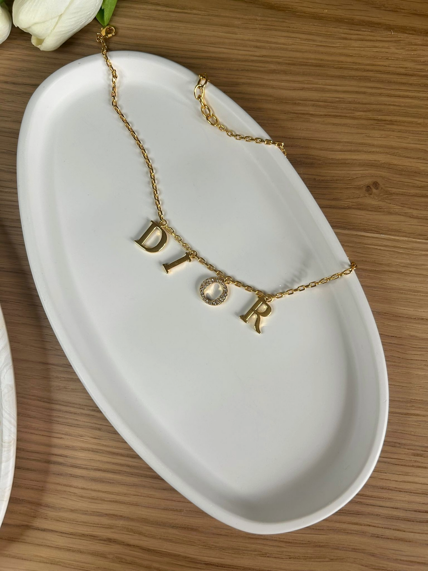 Sleek white oval trinket dish featuring a Dior gold necklace, presented on a wooden table for a refined and luxurious aesthetic.