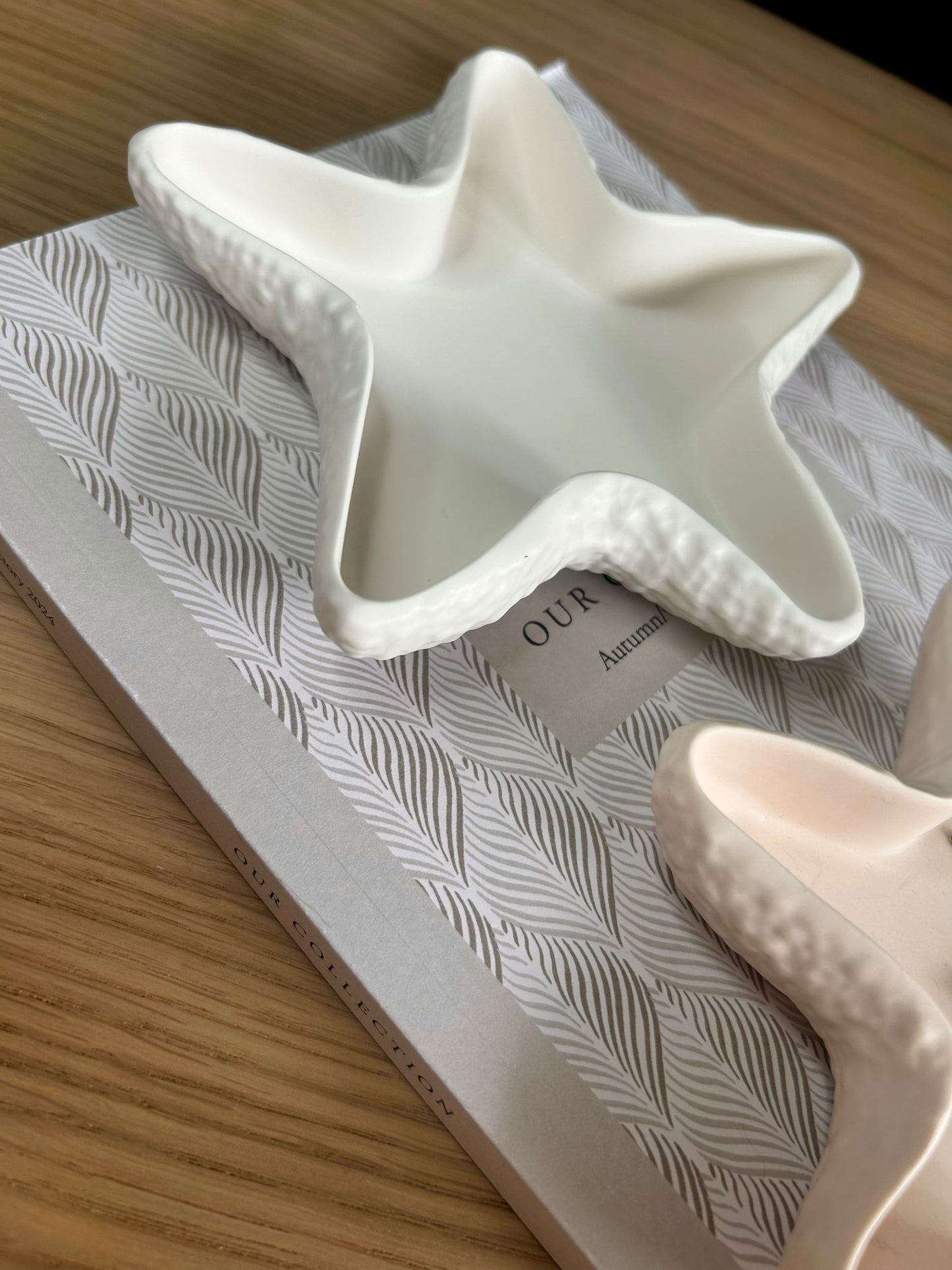 Close-up of a white jesmonite starfish shaped trinket dish with textured edges, positioned on a leaf-patterned book cover, ideal for showcasing handmade and eco-friendly home décor.