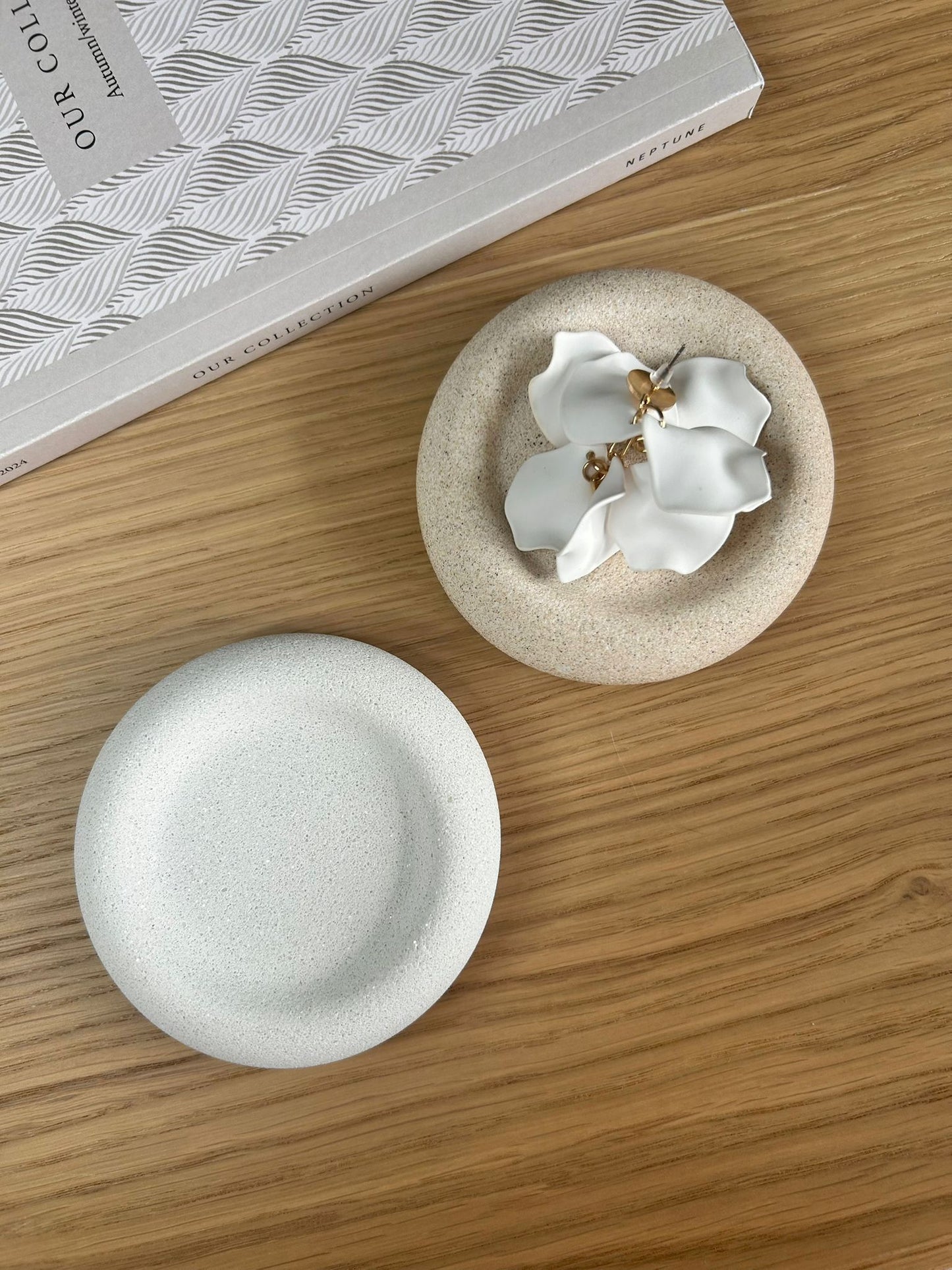 Pair of round speckled Jesmonite trays, one styled with sculptural white floral earrings. Elegant handmade home accessories perfect for bedside or dressing tables.