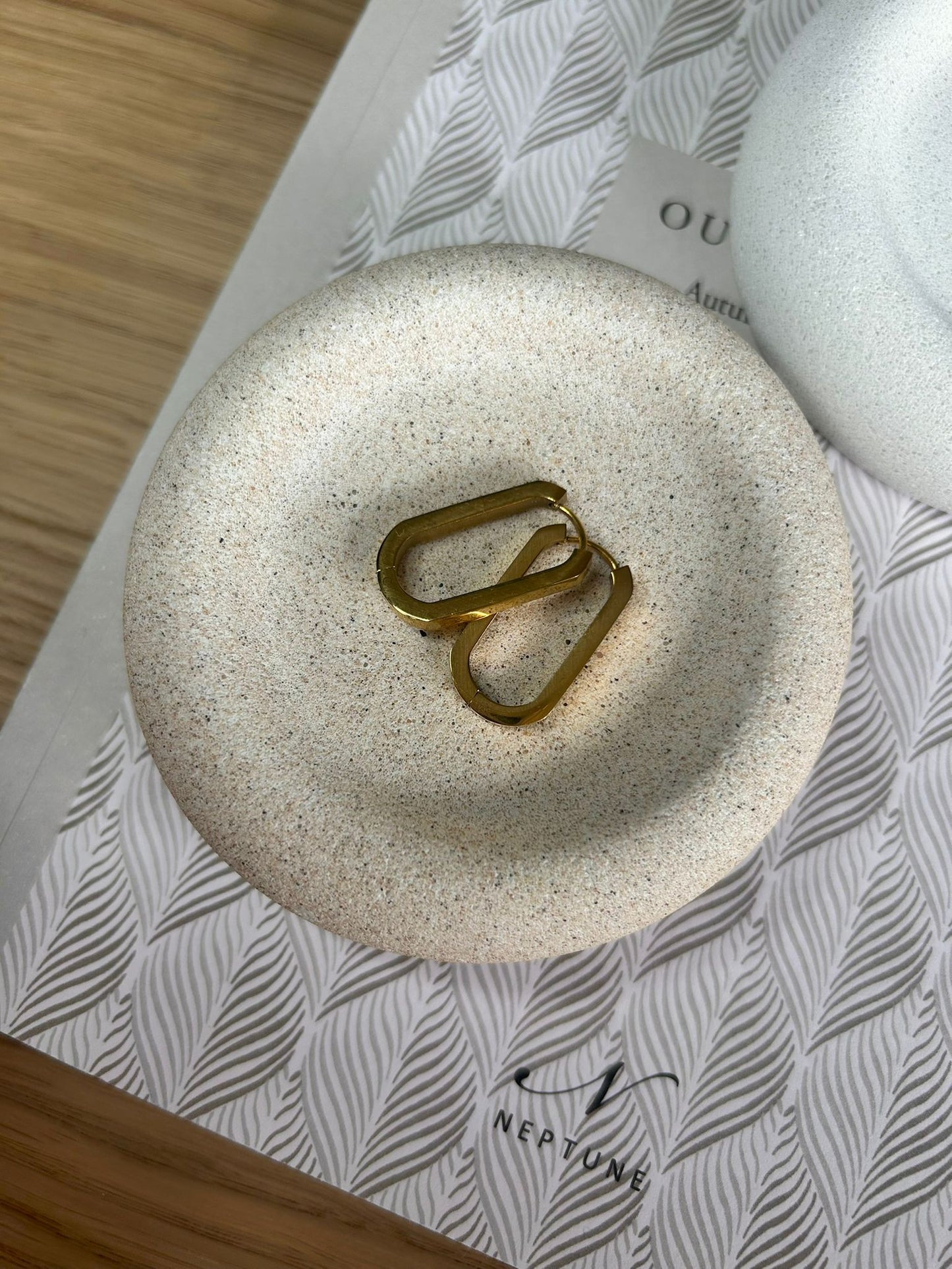 Close-up of a beige speckled handmade Jesmonite tray styled with gold earrings. A minimalist and sustainable home accessory for jewellery or small trinkets.
