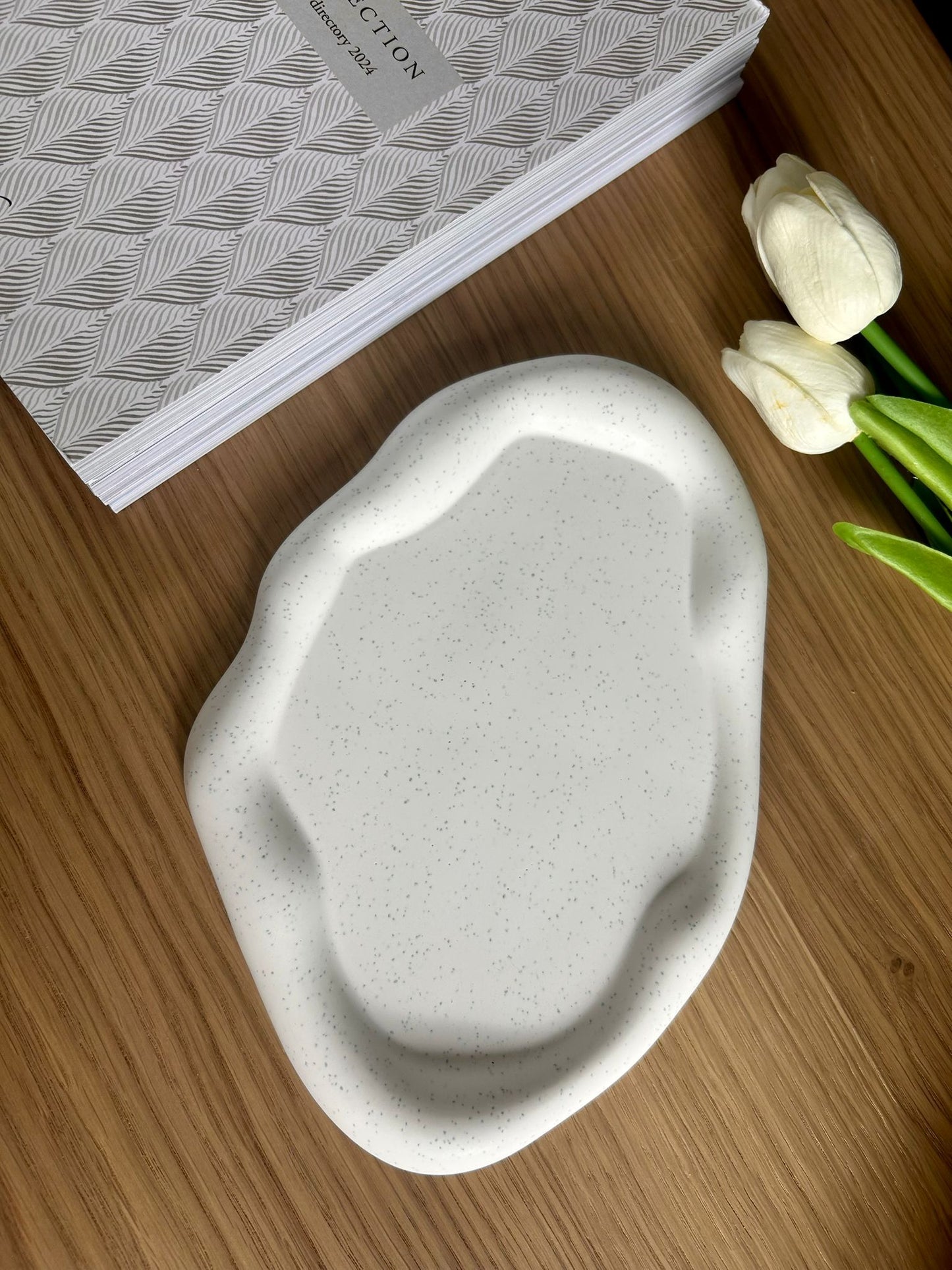 Single speckled Jesmonite tray with organic shape and soft matte finish, placed beside faux white tulips and a decorative journal – a minimalist handmade home accessory
