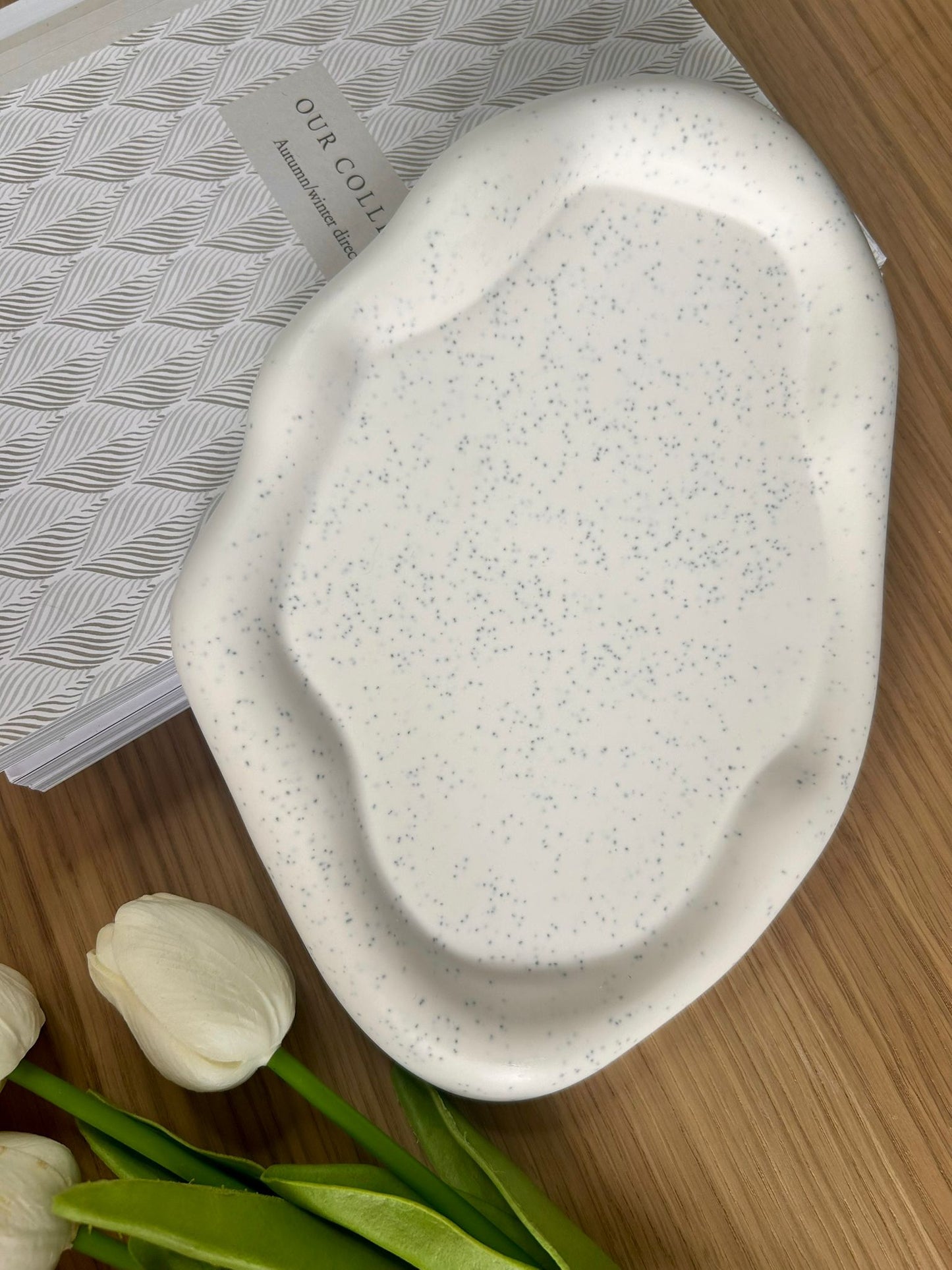Handmade speckled Jesmonite tray with a natural cream base and black flecks, styled with white tulips and a patterned journal – a modern eco-friendly home accessory