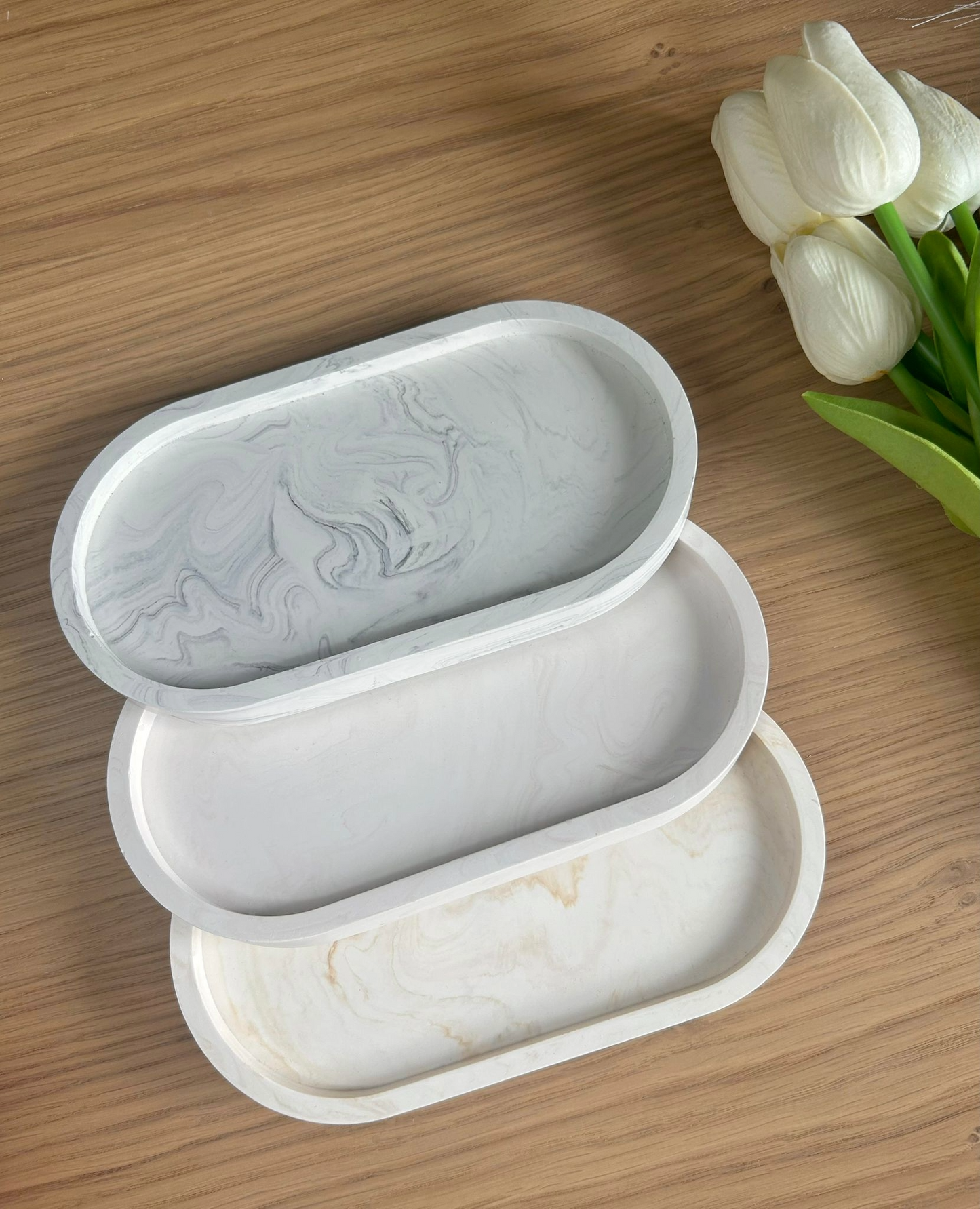 Handmade Jesmonite trays in grey, white, and beige marbling, arranged with white tulips. Stylish, eco-conscious home accessories for jewellery or keys.