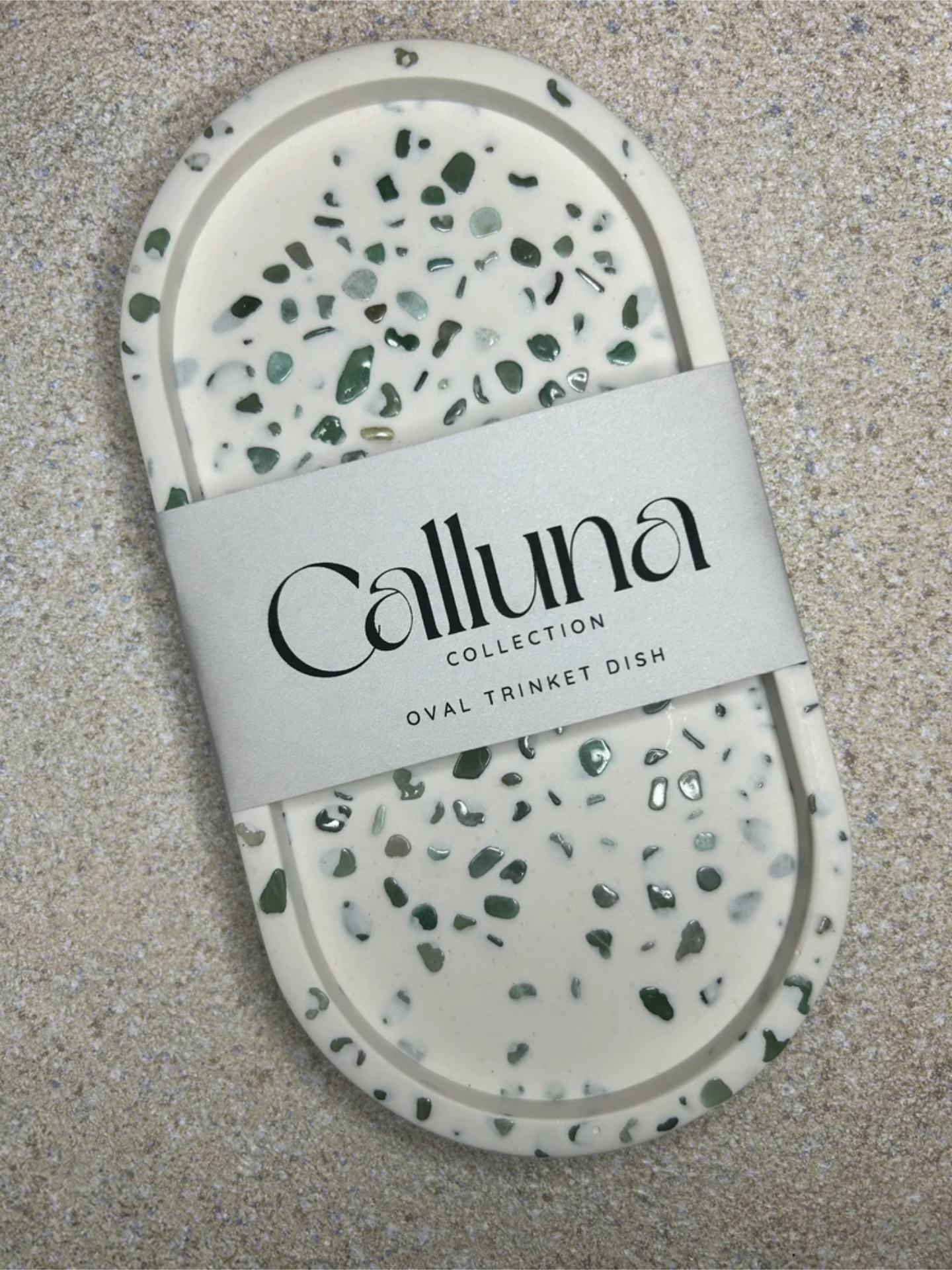 Handmade Home Accessories - A Aventurine Quartz Terrazzo style trinket tray, using real gemstones. It has a belly band around the centre, stating Calluna Colection which is the brand. the photo is designed to show how the item is packaged.