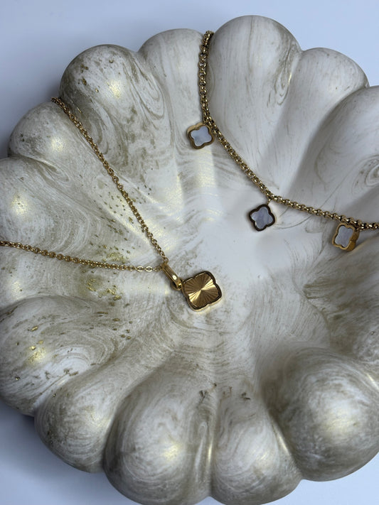 A handmade Jesmonite Celeste Trinket Bowl with a rippled, sculptural edge and soft gold marbled detailing, holding a delicate gold necklace with clover-shaped charms. The bowl’s smooth matte finish and organic form create an elegant, minimalist display on a neutral background.