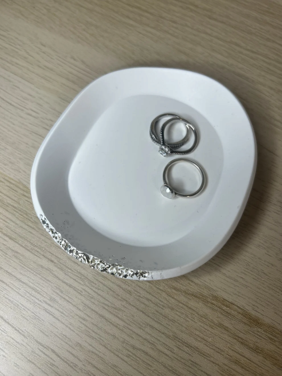 Handmade Home Accessories - An angled shot of an oval style white trinket dish, displaying rings and showcasing it's raw silver druzy style edge.