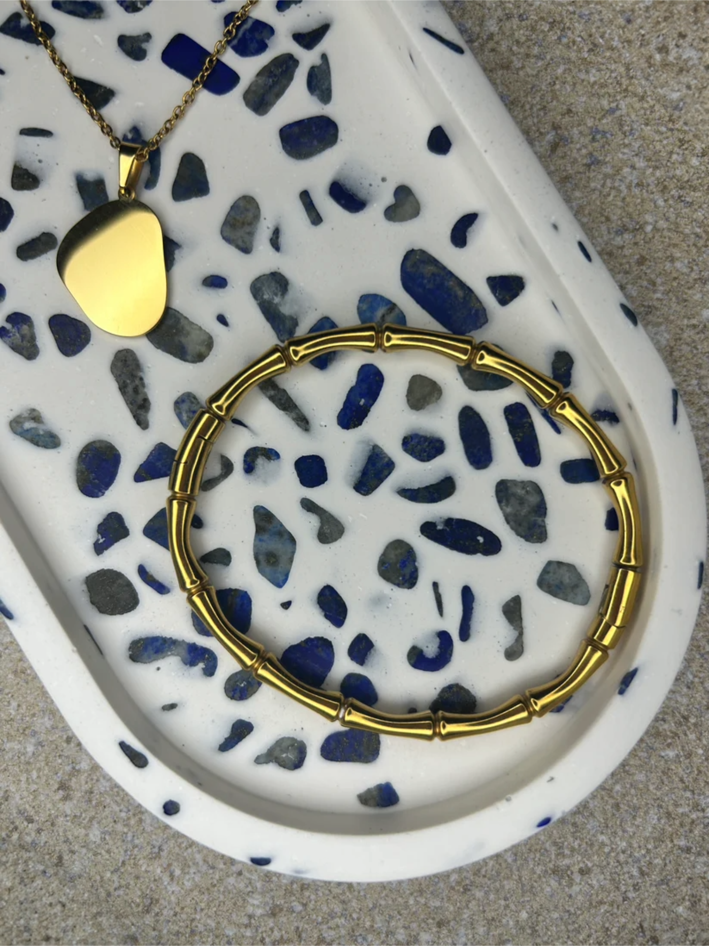 Handmade Home Accessories - A close up shot of a blue and white lapis Lazuli gemstone trinket tray, with a gold wishbone bracelet and a gold necklace on for decor purposes.