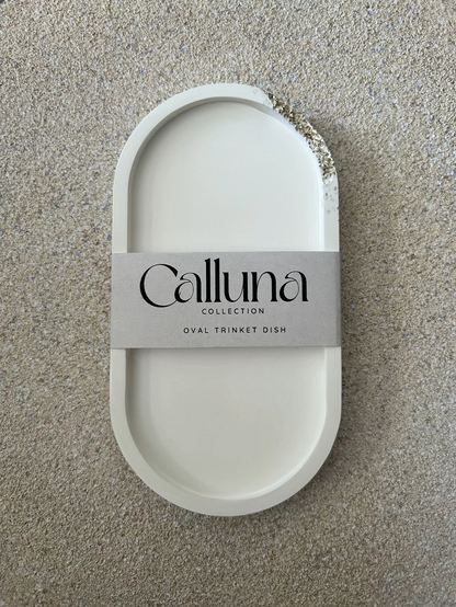 Handmade Home Accessories - a vertical front on shot of a white oval trinket tray with silver druzy details in the top right corner, it has a belly band around the centre stating the brand Calluna Collection.