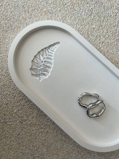 Handmade Home Accessories - A close up shot of a white trinket tray with a fern leaf in silver foil, it has a pair of silver hoops on for display purposes.