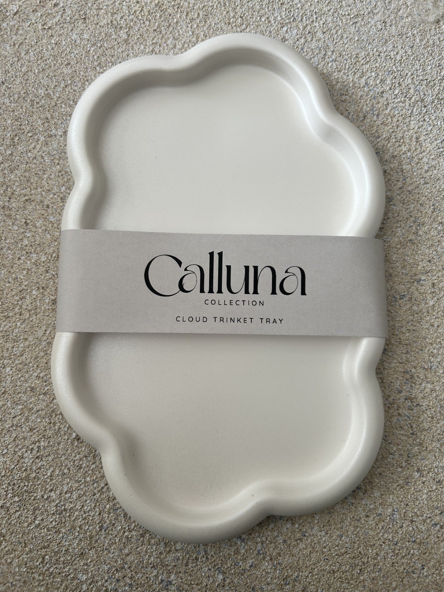 Handmade Home Accessories - A photo of a cloud trinket tray in white, with a belly band wrapped around the middle that states the brand name Calluna Collection. This photo is designed to show how the piece will come packaged.