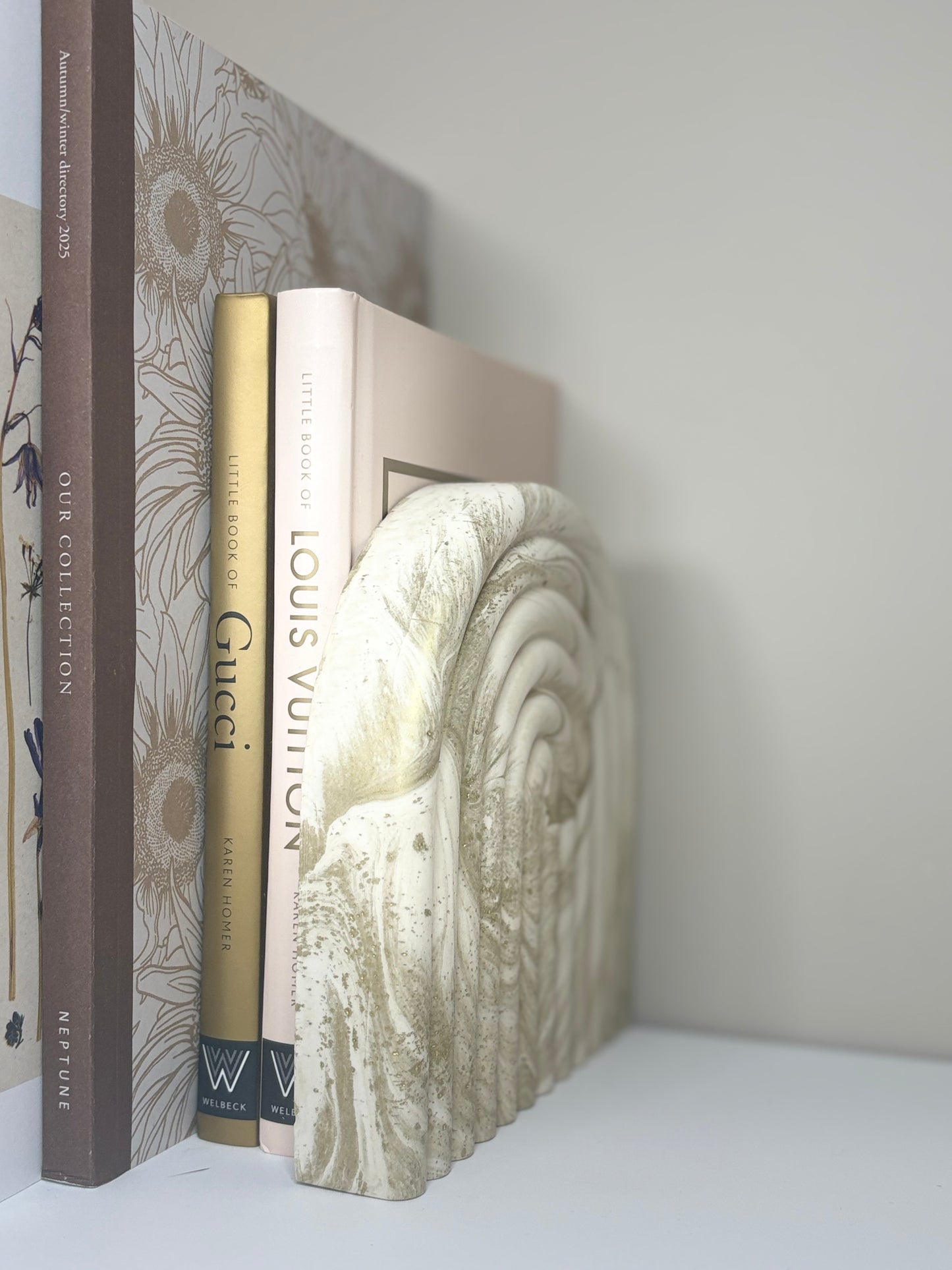 Handmade Luna Arch Bookend crafted from marbled cream and gold Jesmonite, styled beside neutral-toned design books including Gucci and Louis Vuitton, creating a serene and sophisticated shelf display.