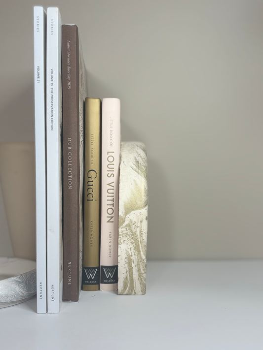 Luna Arch Bookend handcrafted from marbled cream and gold Jesmonite, styled holding neutral-toned design books upright against a minimalist beige backdrop for a serene, sculptural display.