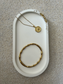 Handmade Home Accessories - Veritcal shot of a oval white trinket tray, with a raw gold druzy style corner edge, with a gold necklace and gold wishbone bracelet on for display.