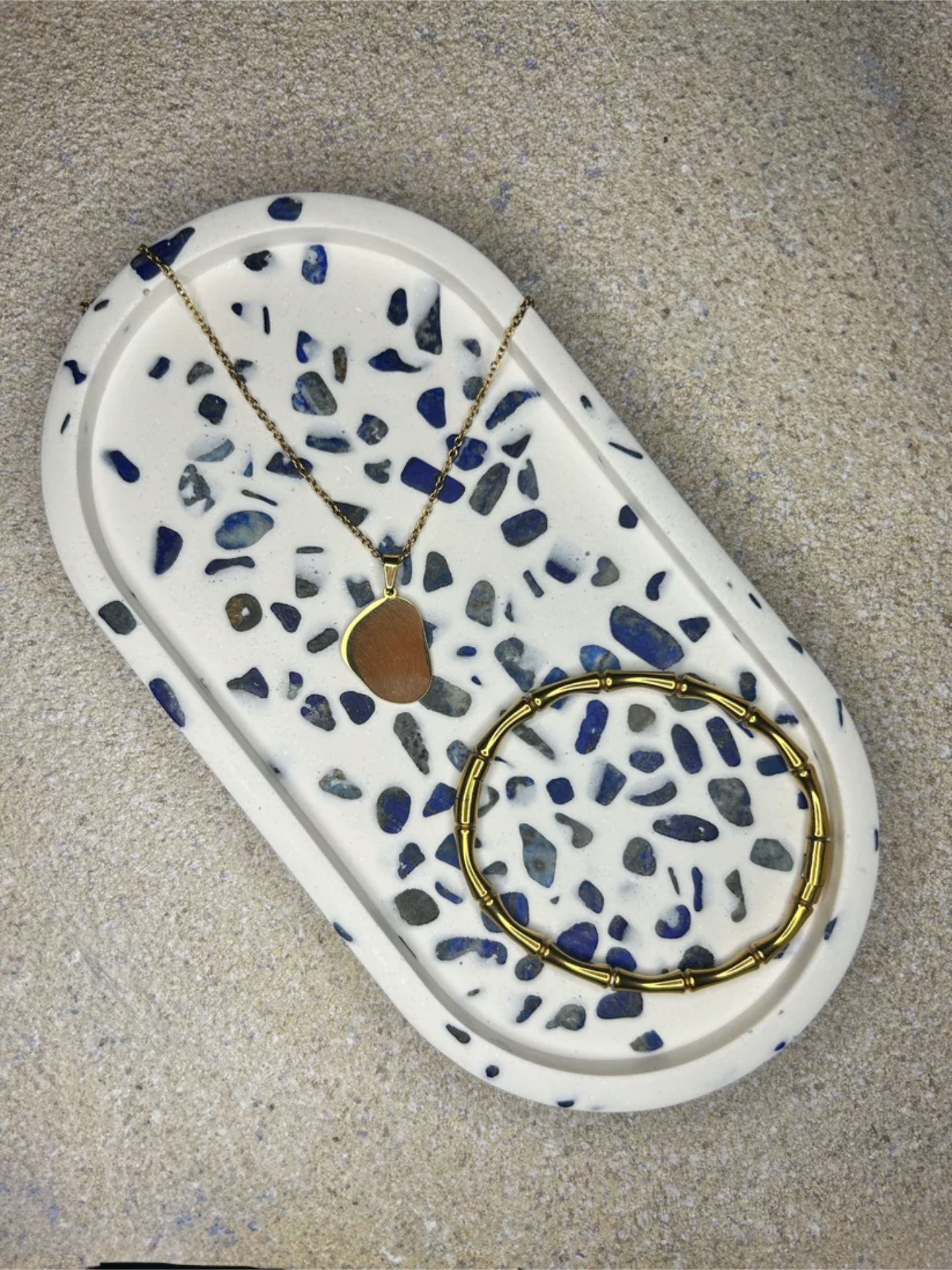 Handmade Home Accessories - A Blue and white oval shaped trinket dish made of lapis lazuli gemstones with a gold wishbone bracelet and a gold necklace on for decor purposes.