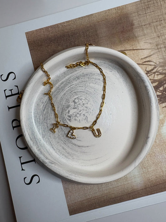 A handmade neutral Jesmonite trinket dish with a soft marbled swirl design, styled on a book with a delicate gold necklace featuring letter charms.