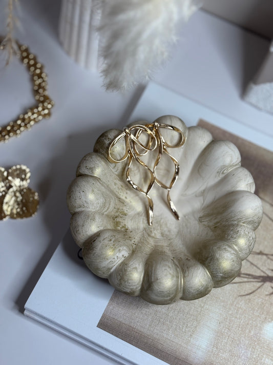 A handmade Jesmonite Celeste Trinket Bowl with a softly rippled edge and delicate gold marbled detailing, displayed on a neutral book with gold jewellery resting inside. The bowl features a sculptural, organic shape that adds a touch of luxury and elegance to minimalist home décor.