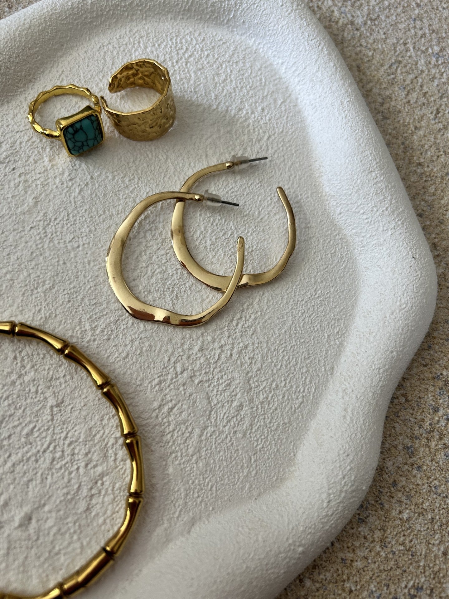 Handmade Home Accessories - Close up of a white textured pebble tray, used to show detail and texture. It has 2 gold rings, a bracelet and gold hoop earrings on.