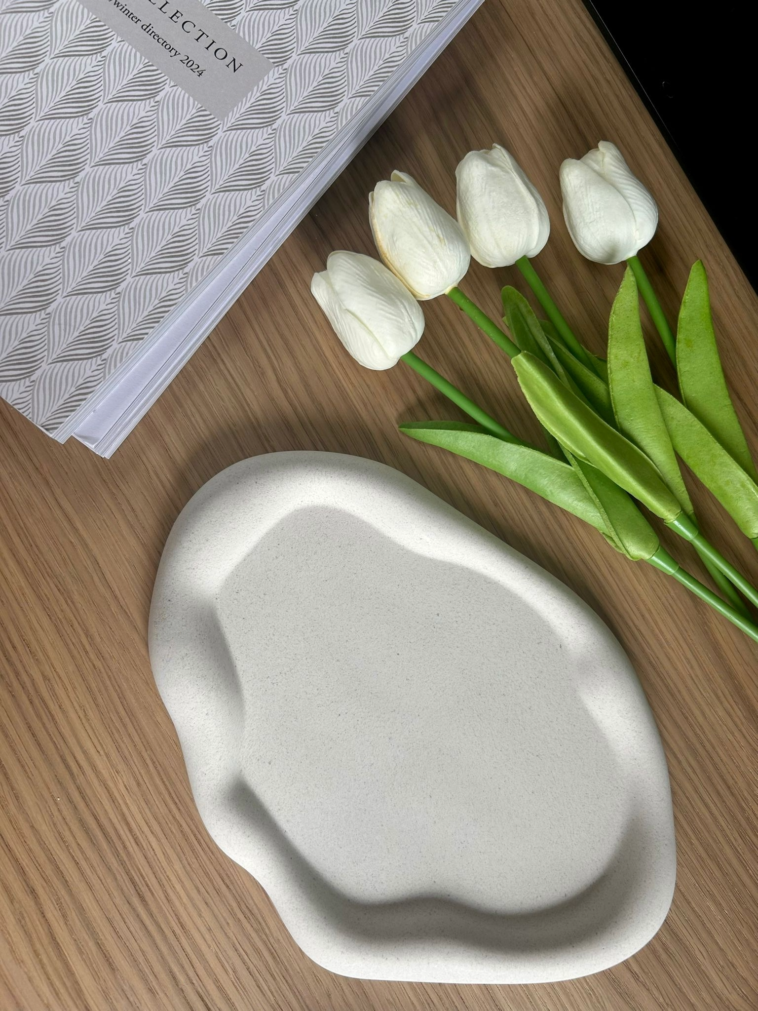 Contemporary handmade ceramic dish with a fluid form, styled with white tulips and a textured journal – perfect for eco-conscious home styling