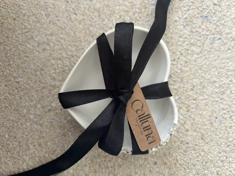 Handmade Home Accessories - A white heart trinket dish with a druzy style raw silver edge, with black ribbon wrapped in a bow that has a tag on that says the company name Calluna Collection.