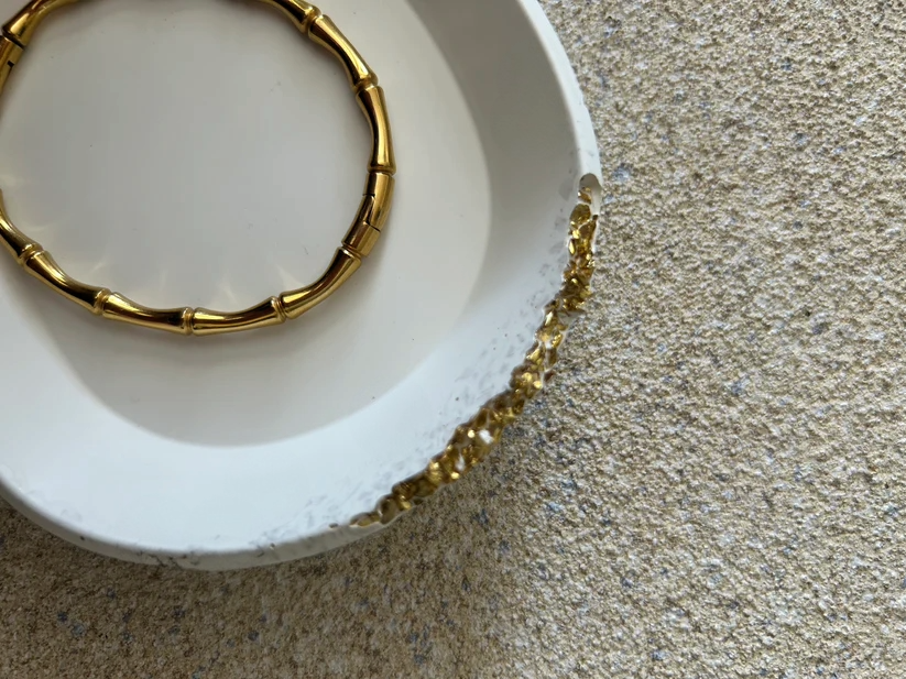 Handmade Home Accessories - a close up shot of a white oval trinket tray with a gold raw druzy edge displaying a gold wishbone style bracelet.