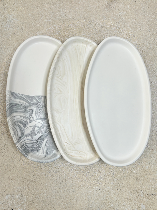 Handmade home accessories - three curved trinket trays, one beige marble, one pure white and one half and half with white and black marble sitting on a stone textured table top