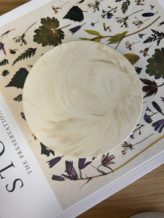 Round beige marbled Jesmonite coaster styled on a floral print book – elegant handmade home accessory with natural swirling detail.