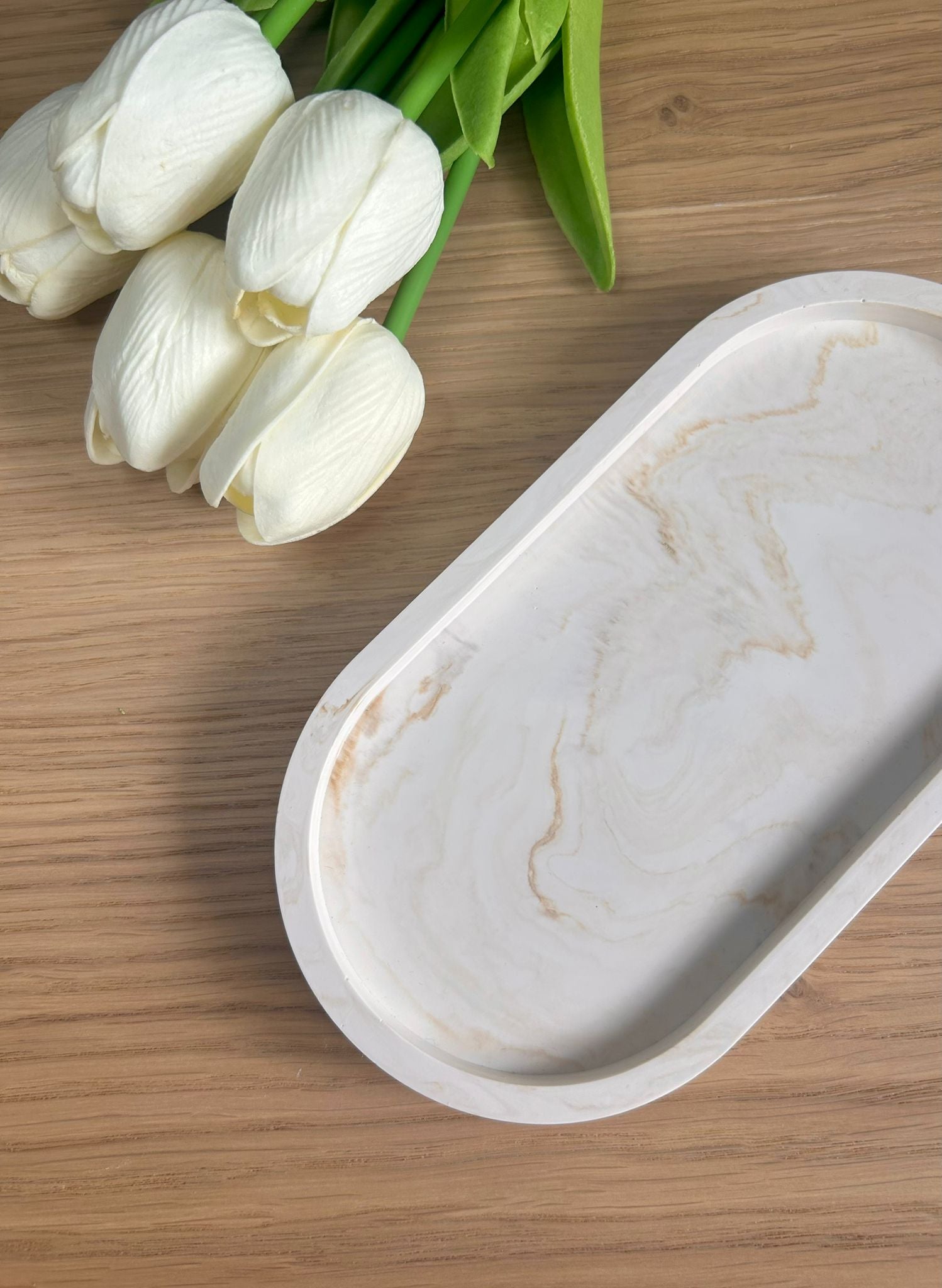 Handmade home accessory – oval Jesmonite tray with a warm marbled finish, styled with faux white tulips on a wooden surface. A beautiful display piece.