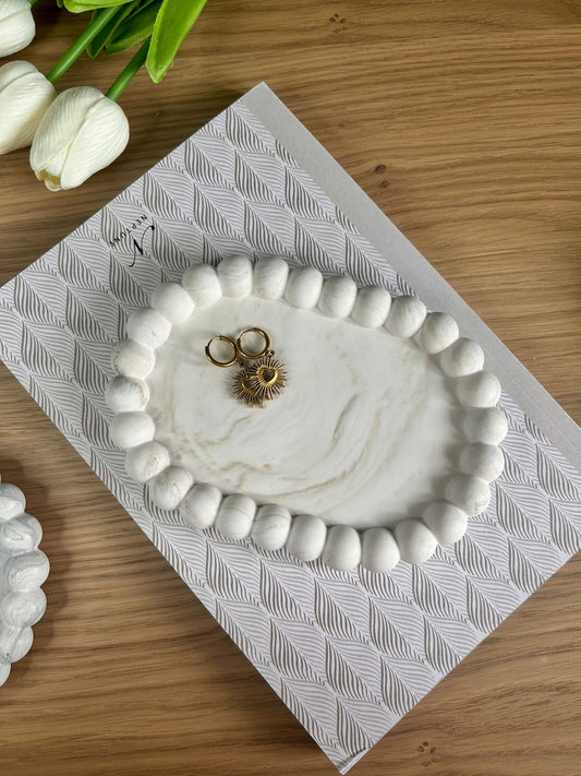 Handmade home accessory – oval Jesmonite tray with pebble edge and soft marble finish, styled with gold jewellery. A sustainable, decorative tray for modern interiors.