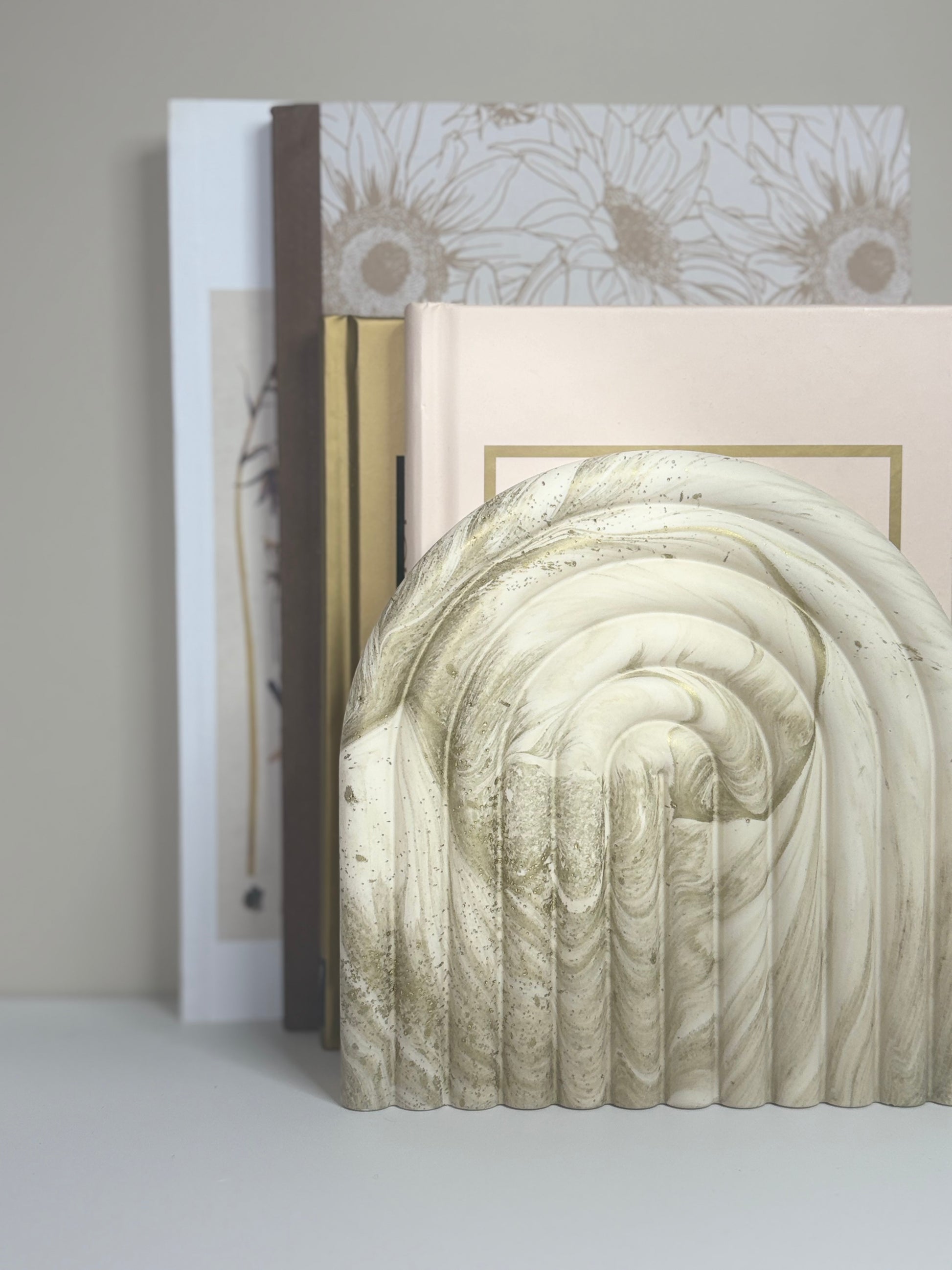 Handmade Luna Arch Bookend in marbled cream and gold Jesmonite, featuring a sculptural arch design with soft curves and textured detailing, styled against a stack of neutral-toned books for a refined, minimalist display.