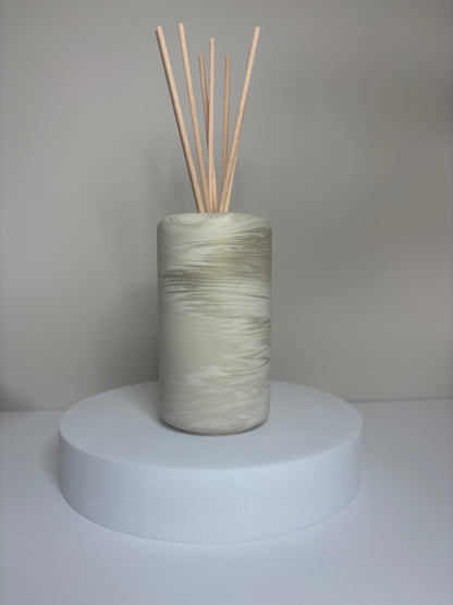 Handmade Solace Diffuser featuring a tall cylindrical Jesmonite vessel with soft marbled tones of beige and stone grey, displayed on a round white pedestal with natural reed sticks.