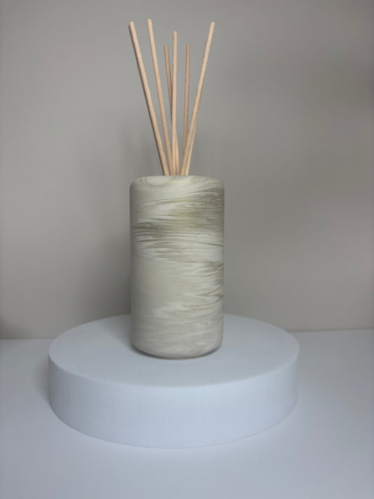 Handmade Solace Diffuser featuring a tall cylindrical Jesmonite vessel with soft marbled tones of beige and stone grey, displayed on a round white pedestal with natural reed sticks.
