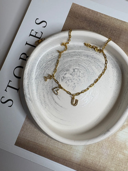 A handmade Jesmonite trinket dish in soft neutral tones with a subtle marbled swirl design, displayed on a book with a delicate gold necklace resting inside.