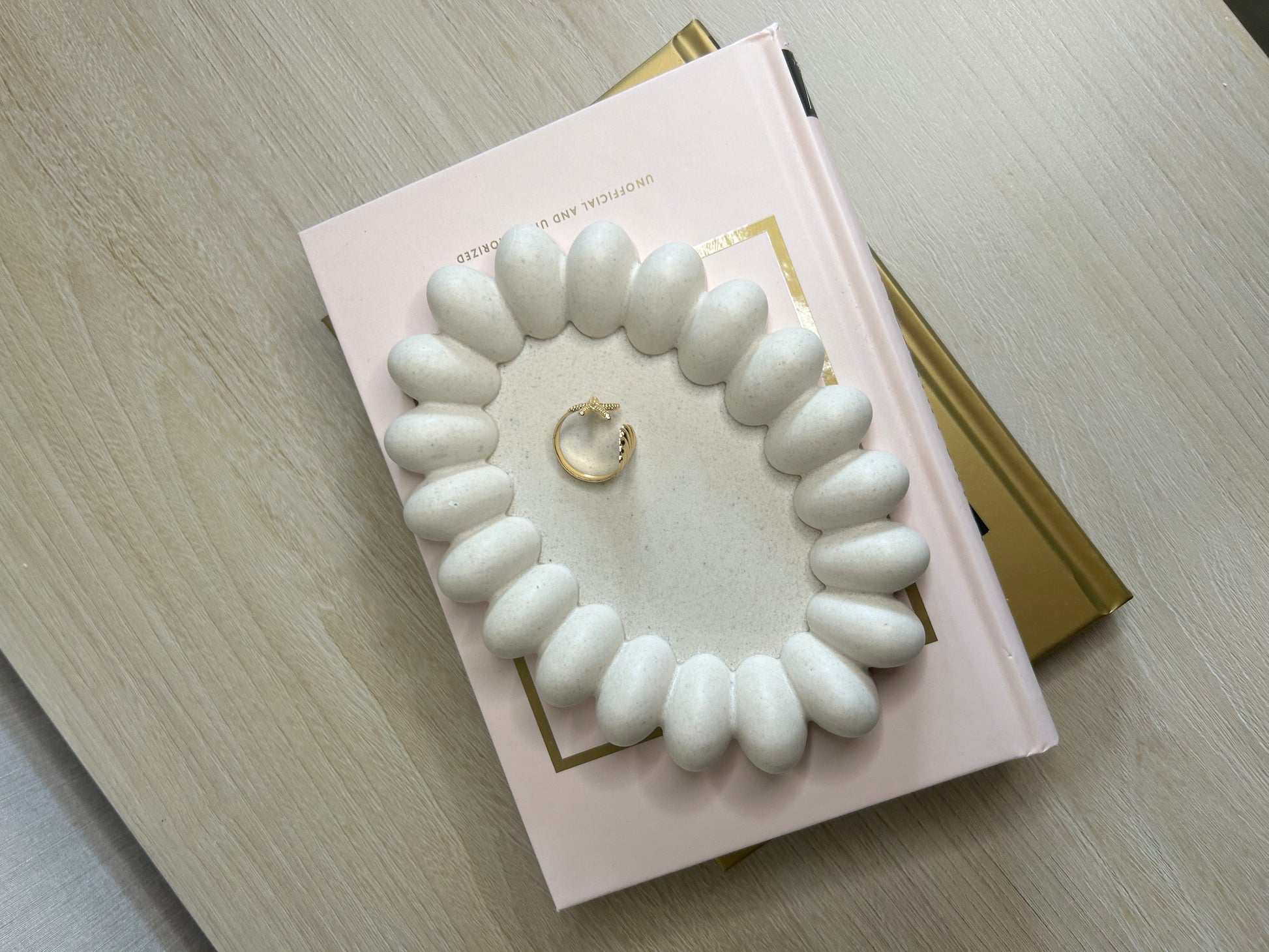 Handmade Home Accessories - A birds eye view shot of the daisy trinket tray on a bedrop of some books. Its oval shape with bubbles around the outside giving the appearance of a daisy.