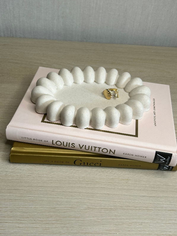 Handmade Home Accessories - A front on shot of the daisy trinket tray, showing the side angle of the bobbles on the outer edge in a natural stone finish, stacked on some books.