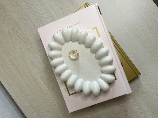 Handmade Home Accessories - A birds eye view shot of the daisy trinket tray on a bedrop of some books. Its oval shape with bubbles around the outside giving the appearance of a daisy.