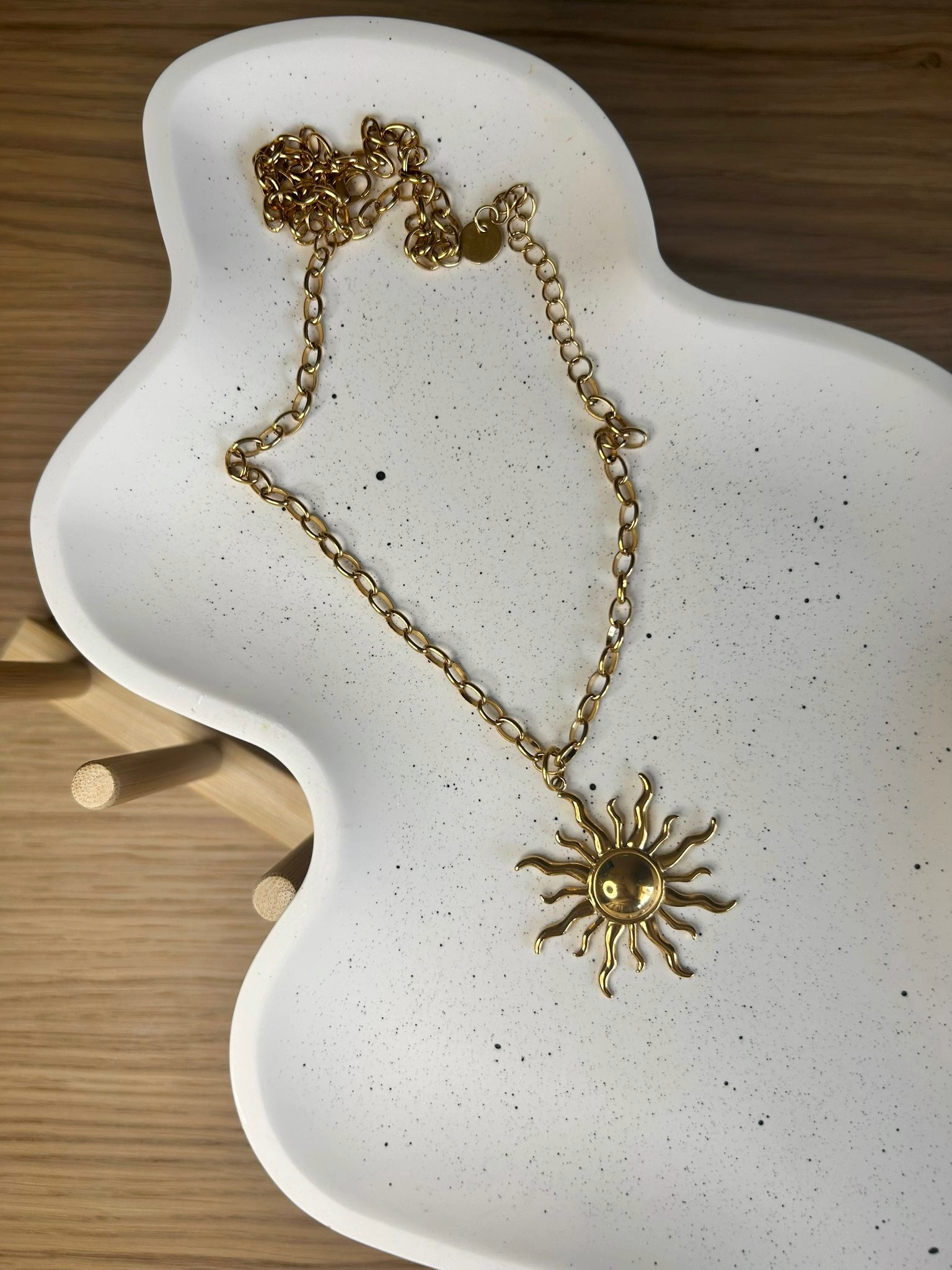 Gold sun necklace displayed on an organically shaped handmade Jesmonite tray with black speckles – elegant styling piece for minimalist interiors.