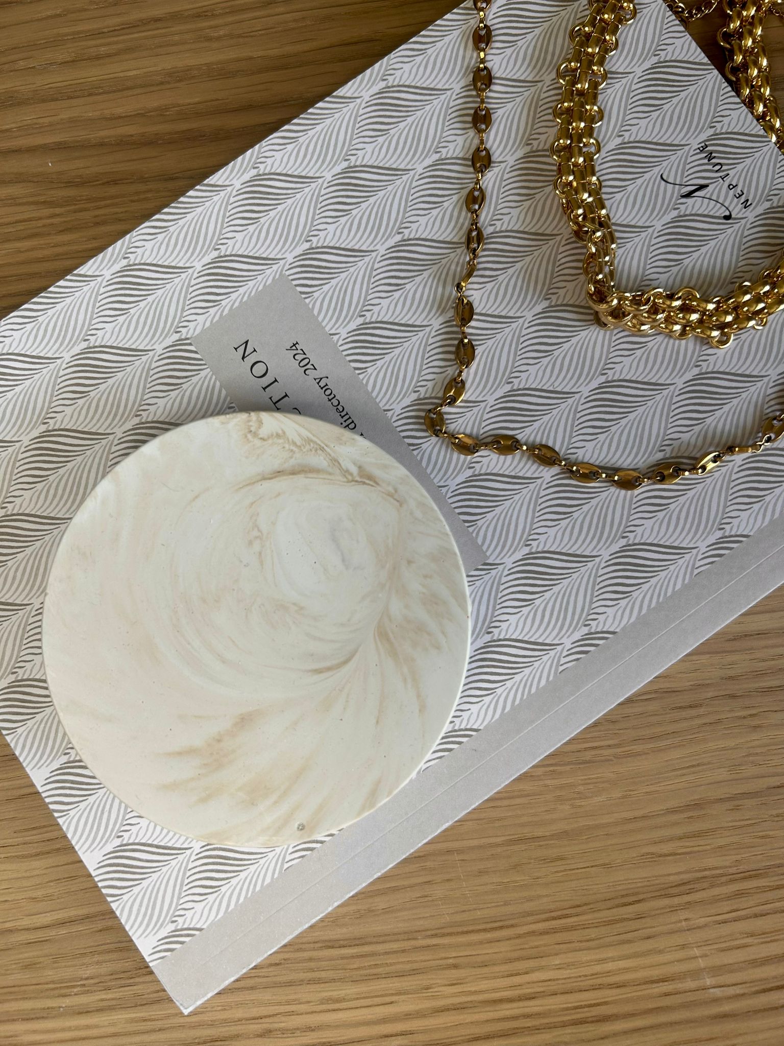 Creamy marbled coaster with soft neutral tones styled beside gold chain jewellery – minimal handcrafted home accessory.