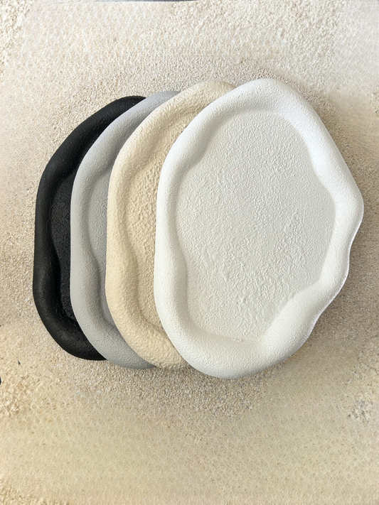 Handmade Home Accessories - four textured pebble style trinket dishes in black, grey, beige and white on a stone textured background.