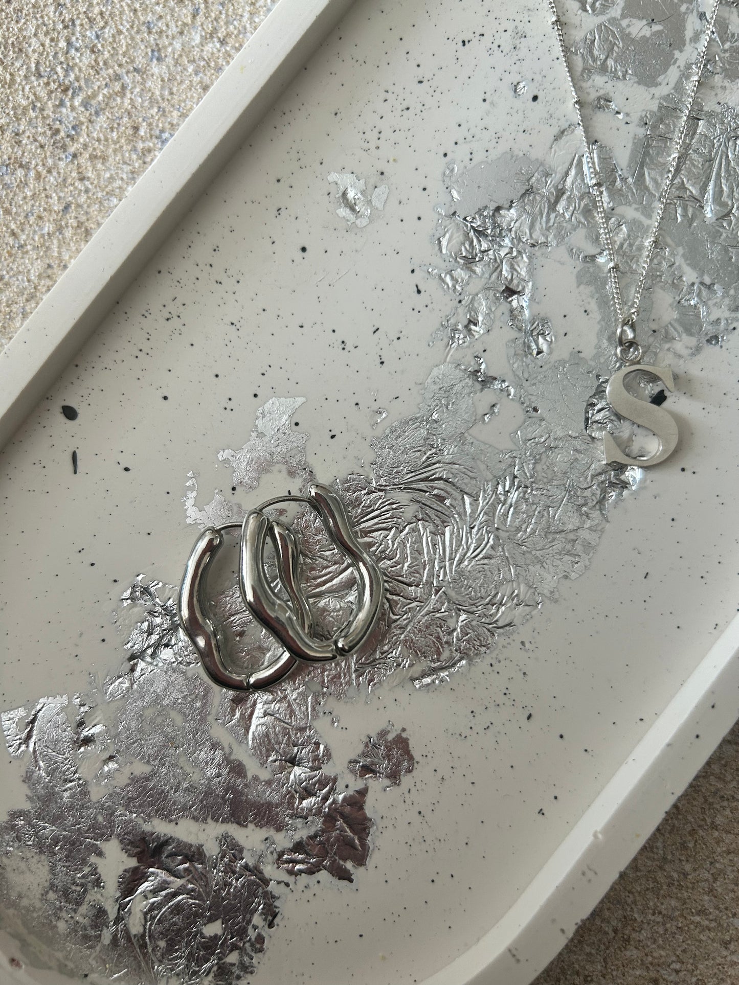 Handmade Home Accessories - A close up shot of a  Large oval cream trinket tray with black splatters and silver leaf detail. Earrings and a silver necklace as on the tray for decorative purposes.