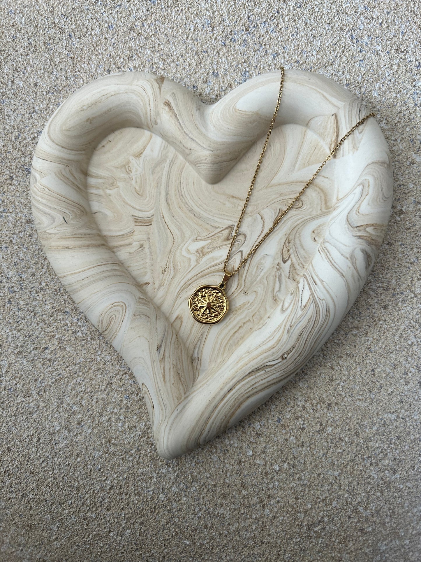Handmade Home Accessories - A beige marble chunky heart trinket dish, on a natural stone backgrounf with a star coin necklace displayed on it.