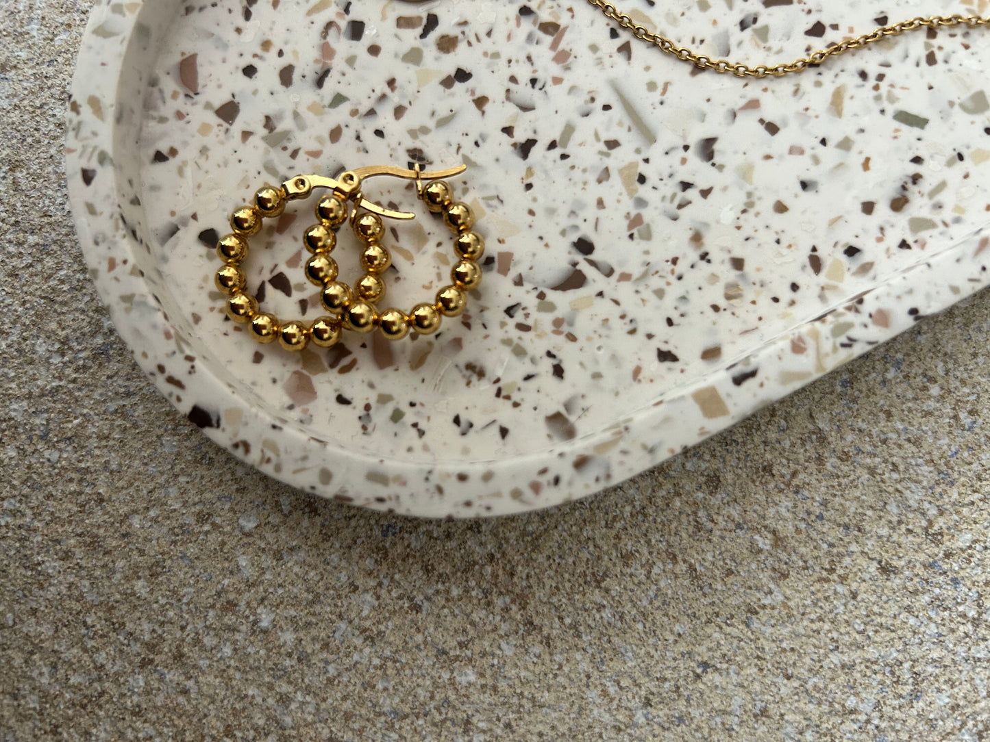 Handmade Home Accessories - A close up shot of an off white terrazzo trinket tray displaying gold hoop earrings.