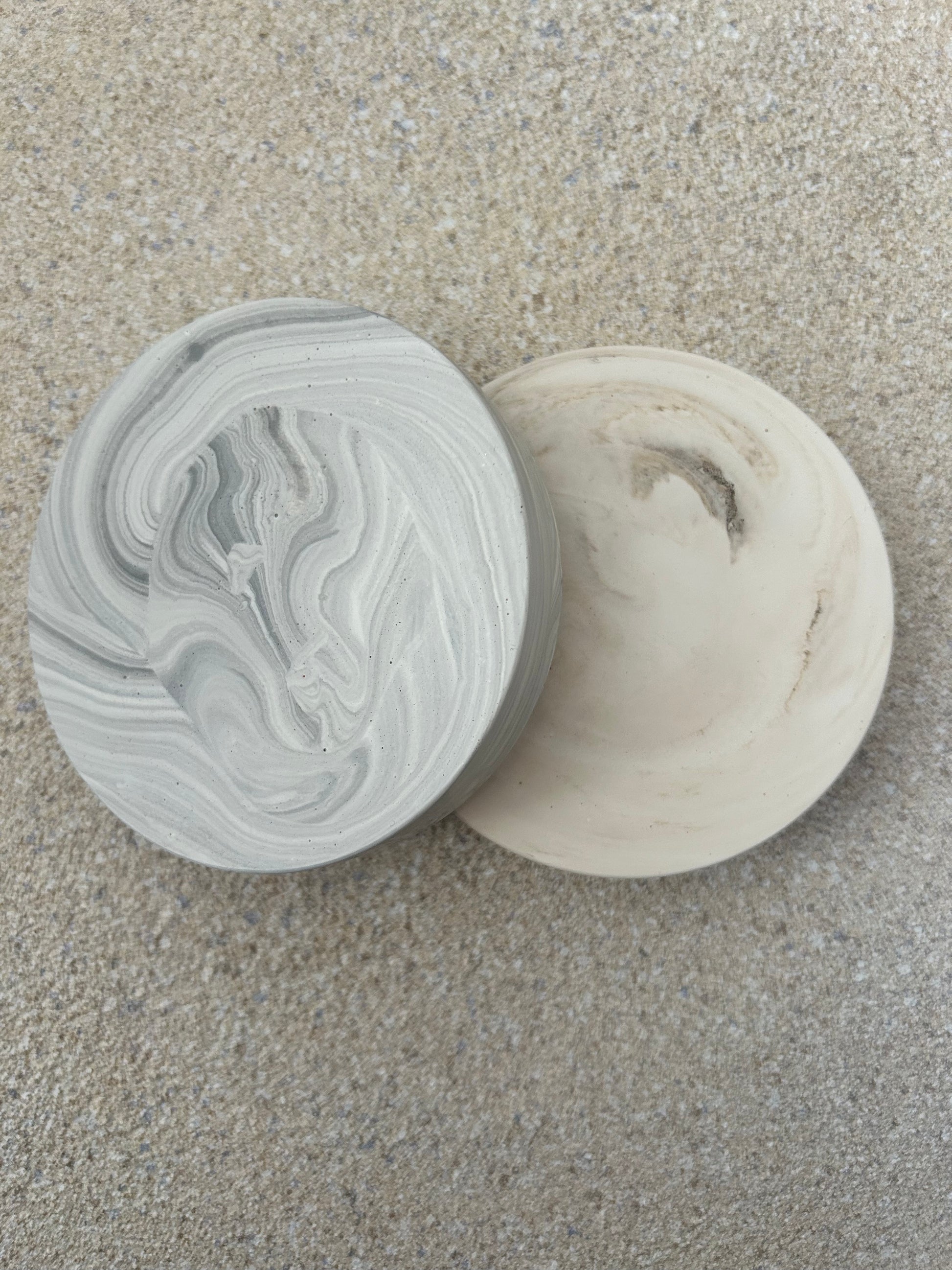 Handmade Home Accessories - two chunky marble coasters one in beige and one in grey stacked together on a textured natural stone background.