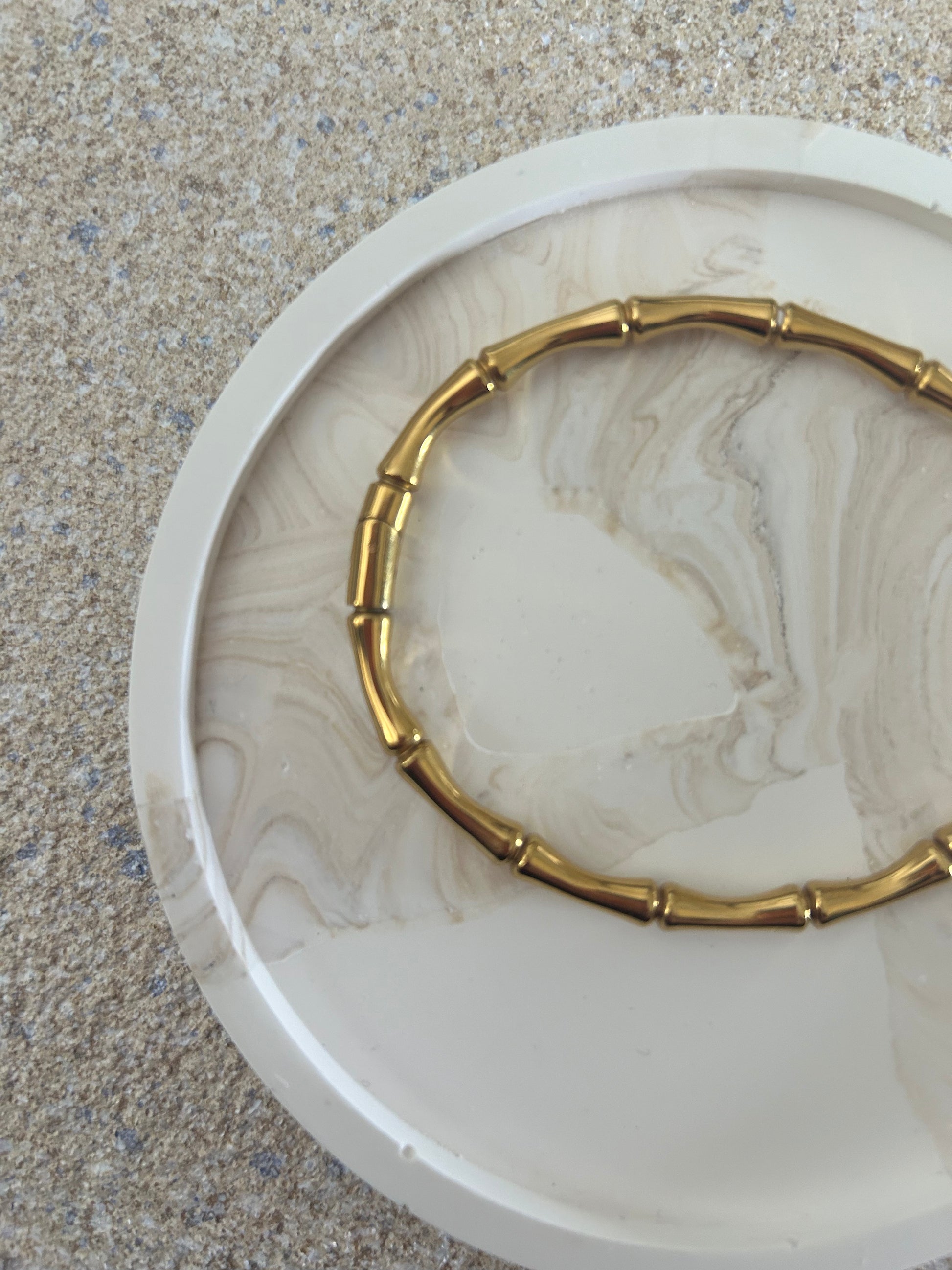 Handmade Home Accessories - A close up shot of a round beige marble and white snap coaster, displaying a wishbone gold bangle.